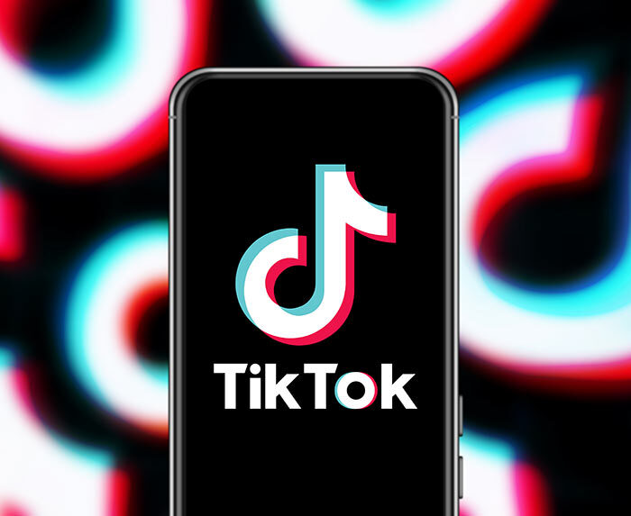 Graphic showing smart phone with TikTok logo on screen and blurry TikTok logo in background